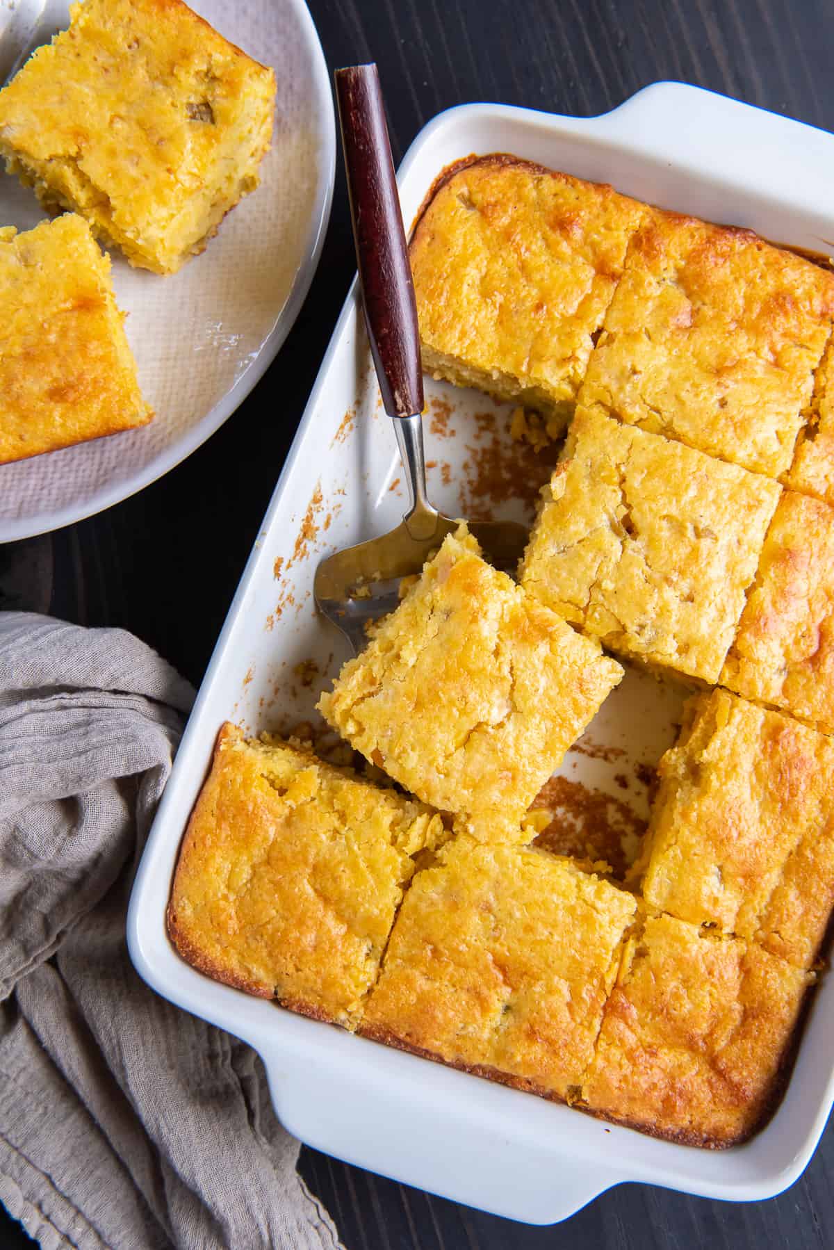 A top down shot of sliced cornbread in a white baking dish with a spatula.