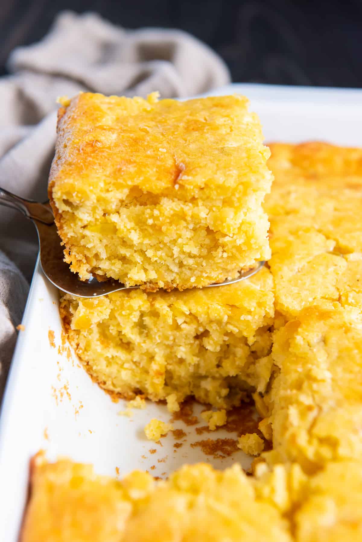 A spatula lifts a slice of Jiffy Mexican Cornbread from a white baking dish.
