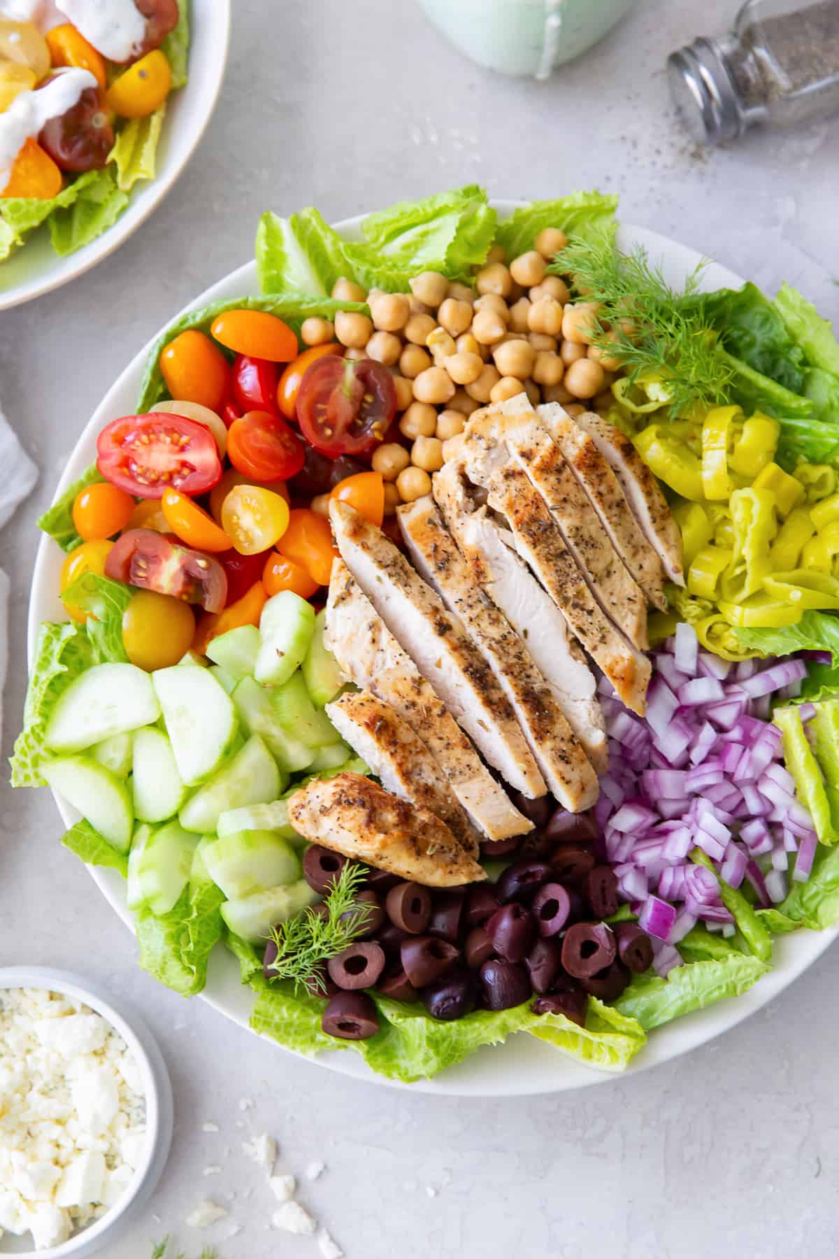 A top down shot of Mediterranean Chicken Salad next to a small bowl of feta and salt and pepper shakers.