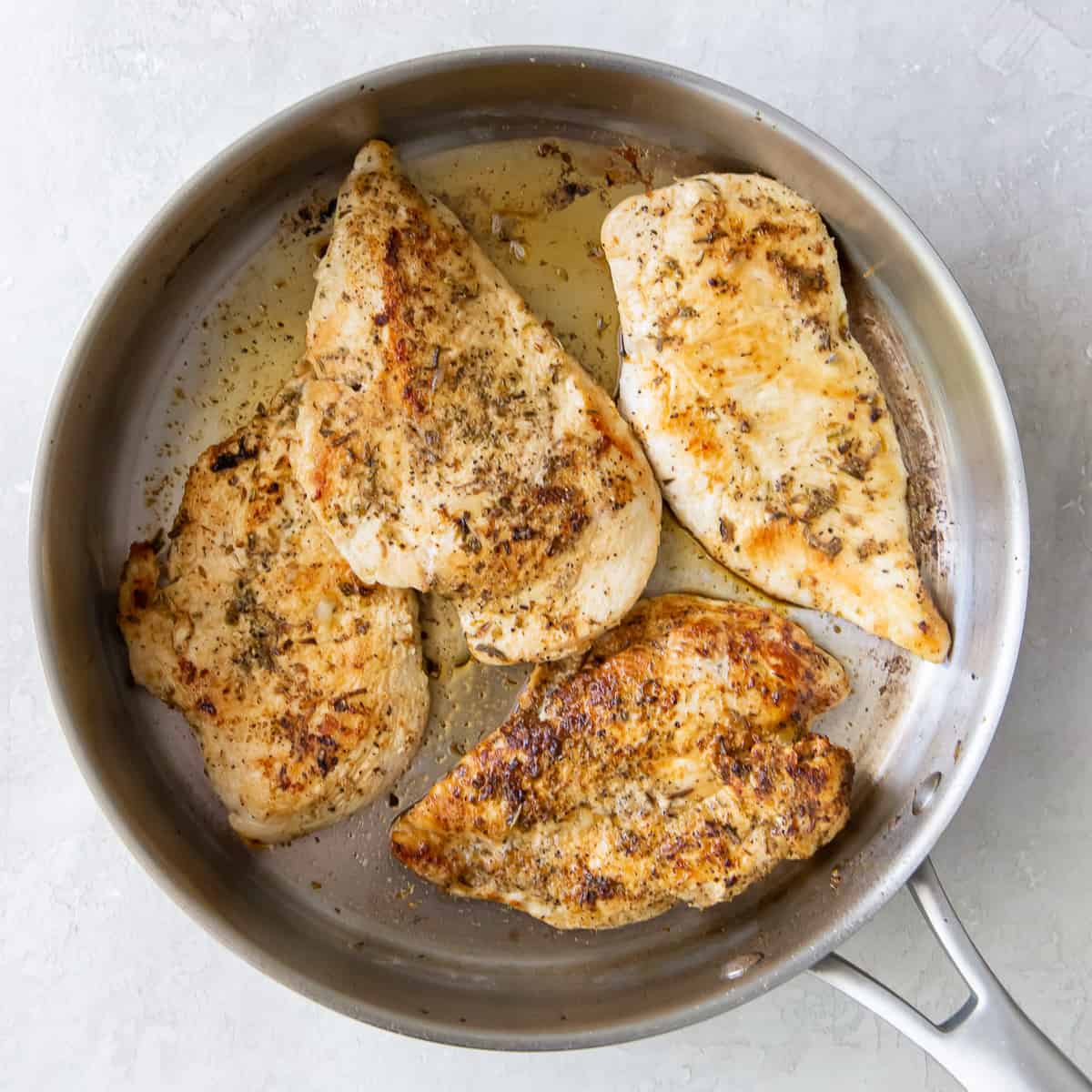 Seasoned chicken breasts cooking in a skillet.