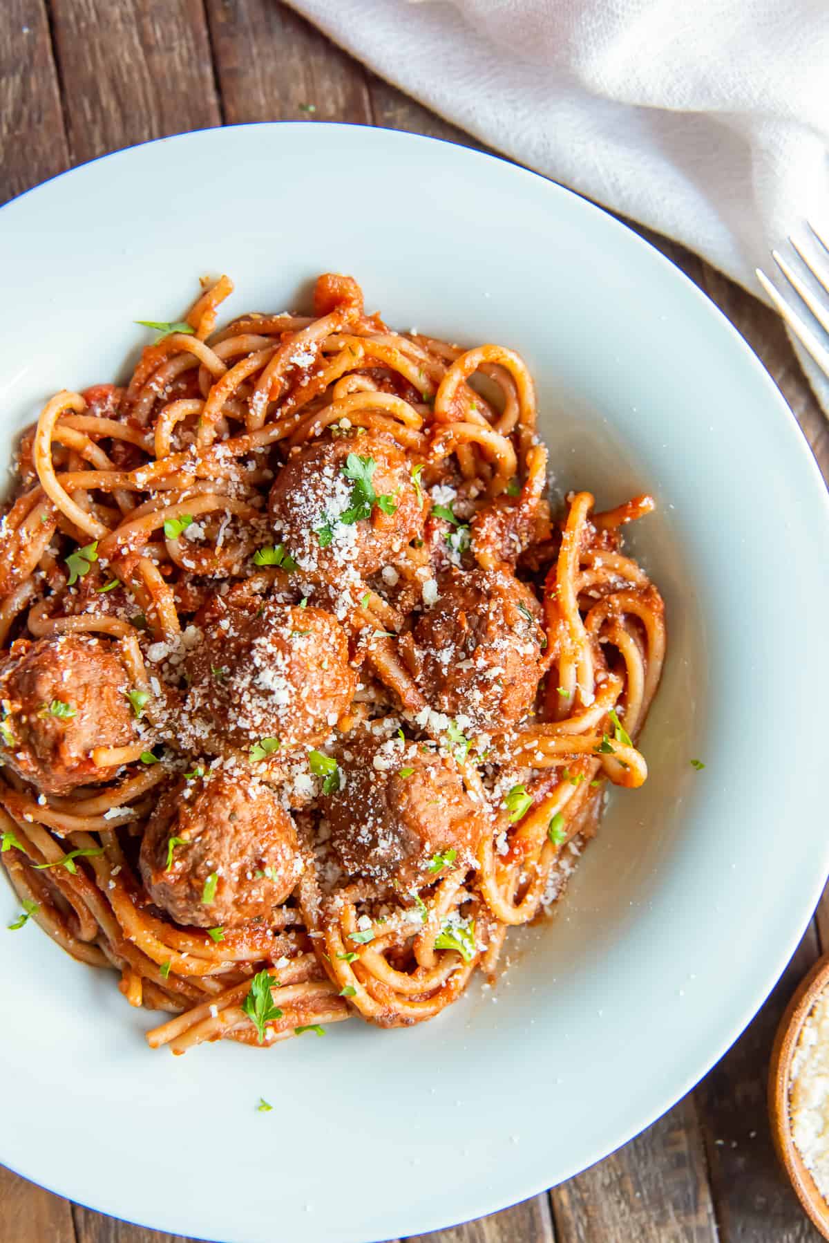 A top down shot of spaghetti and meatballs in a white bowl next to a white and red cloth.