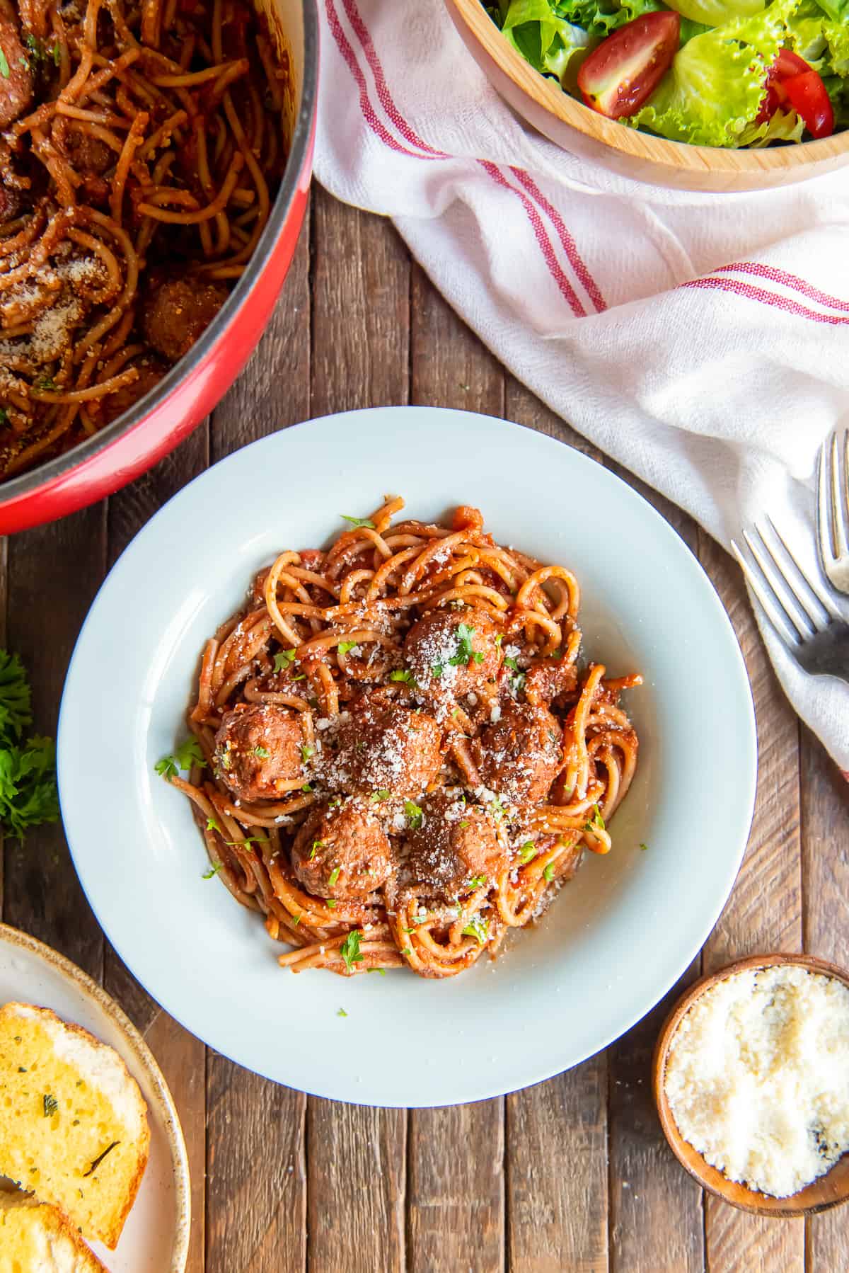 A top down shot of spaghetti and meatballs in a white bowl next to a pot full.