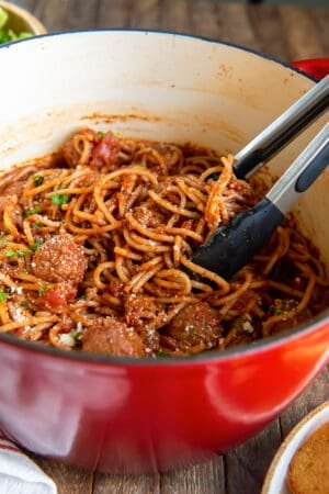 Metal tongs in a pot of spaghetti and meatballs.
