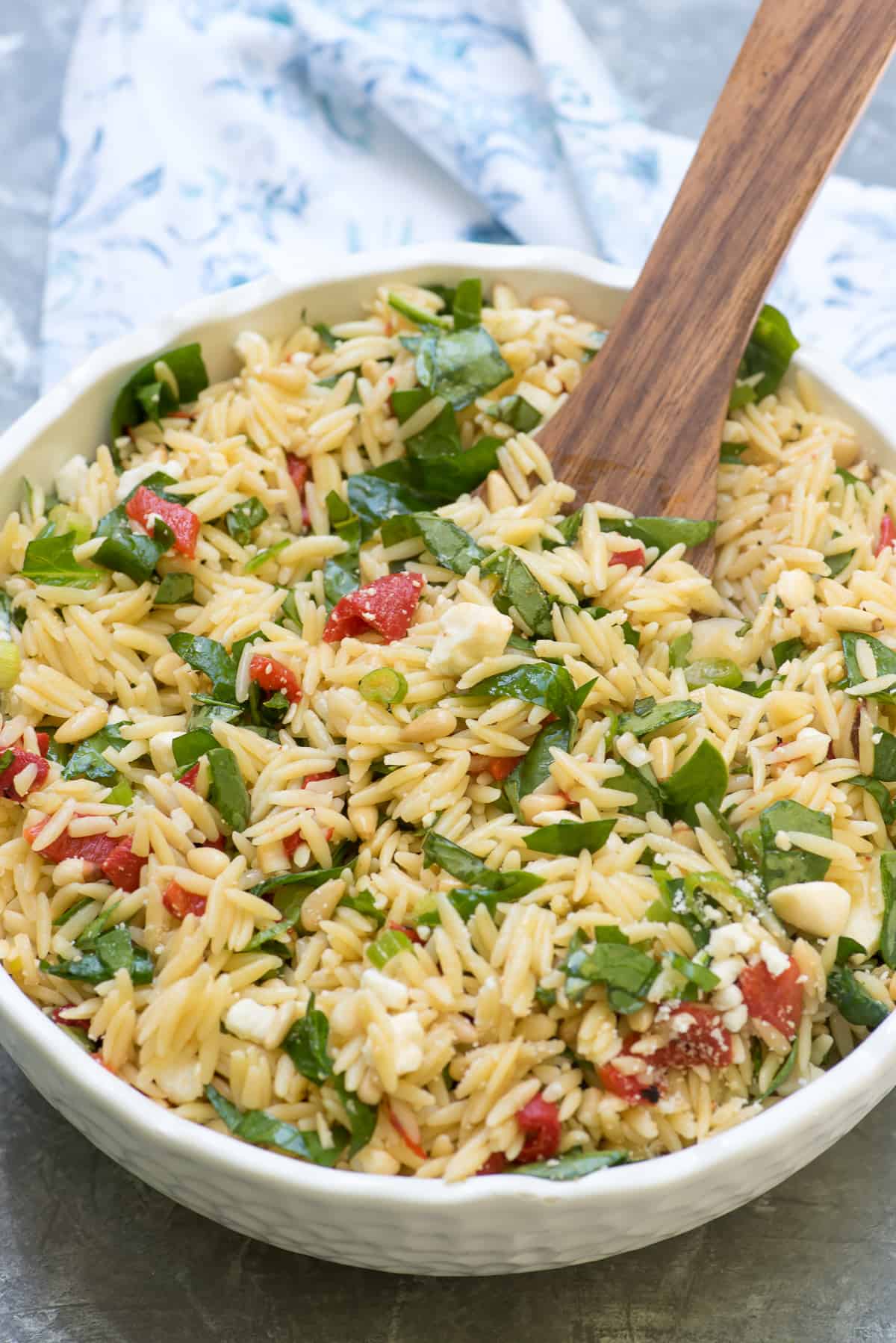 A wooden serving spoon resting in a bowl of orzo salad.