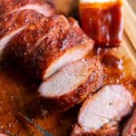 Sliced pork tenderloin on a cutting board with a pastry brush coated in barbecue sauce.