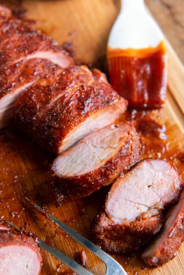 Sliced pork tenderloin on a cutting board with a pastry brush coated in barbecue sauce.