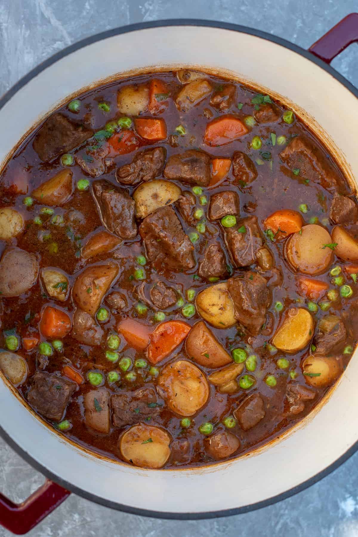 A top down shot of a pot of beef stew with carrots, potatoes, and peas.