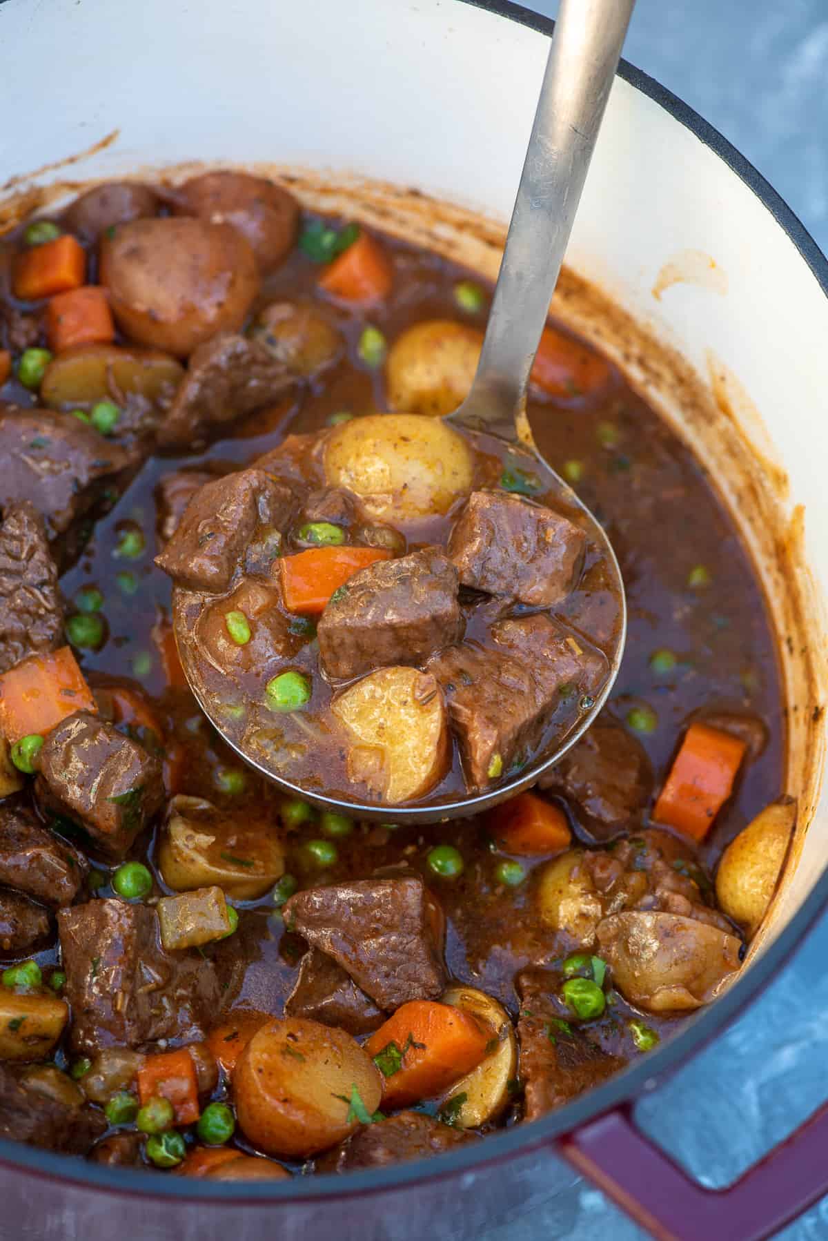A ladle scooping beef stew from a pot.