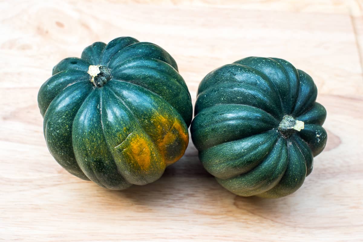 Two green and orange whole acorn squash on a cutting board.