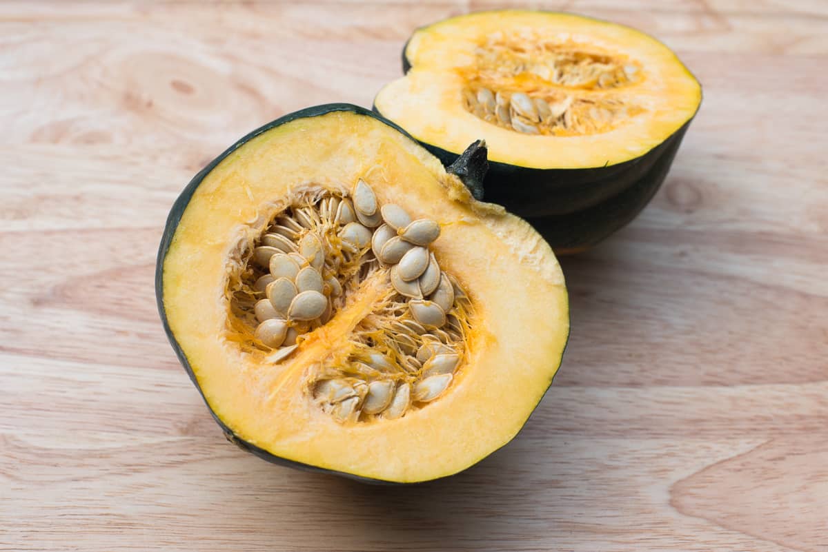 A halved acorn squash with seeds on a cutting board.