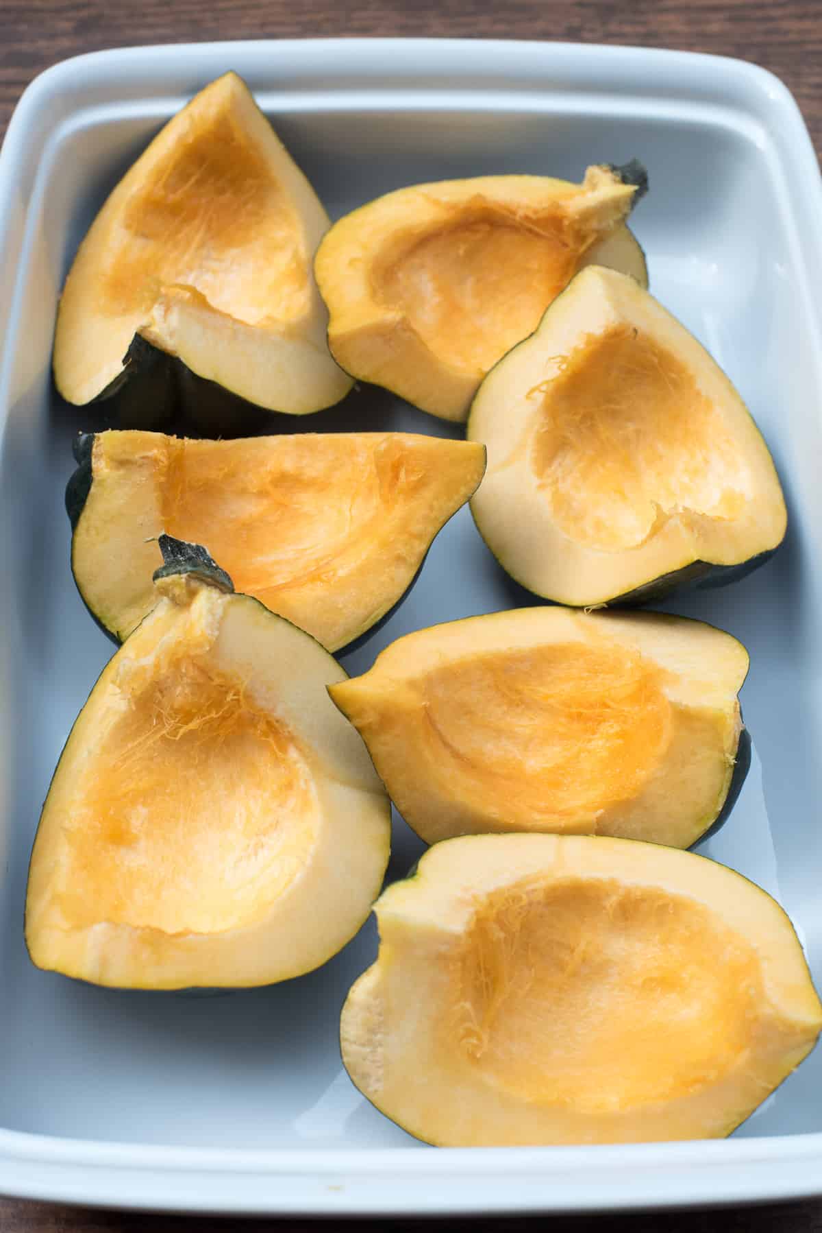 Quartered acorn squash with the seeds removed in a white baking dish.