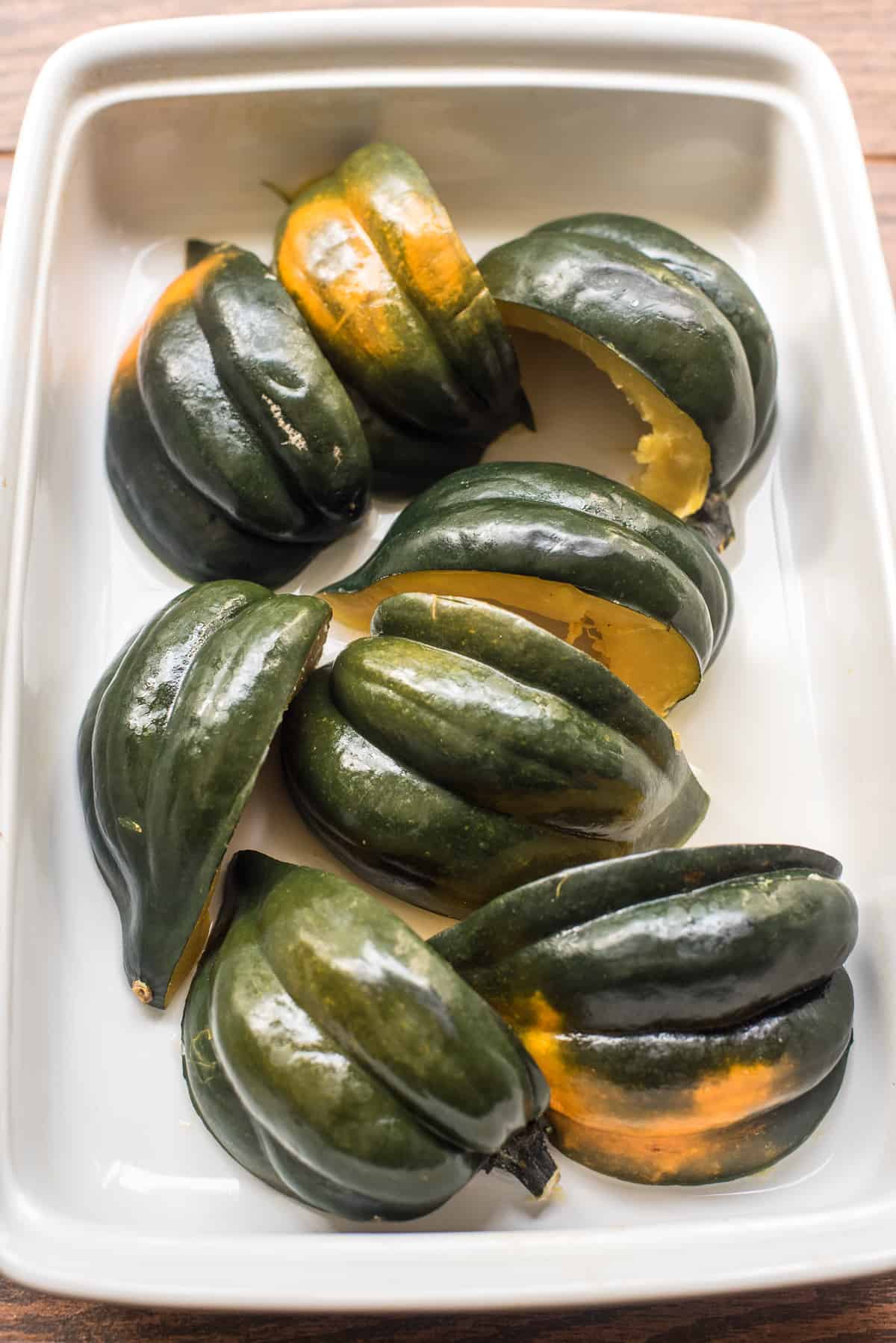 Quartered and baked acorn squash with the skin side up in a white baking dish.