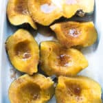 Pieces of sweet baked acorn squash with butter and brown sugar in a baking dish.