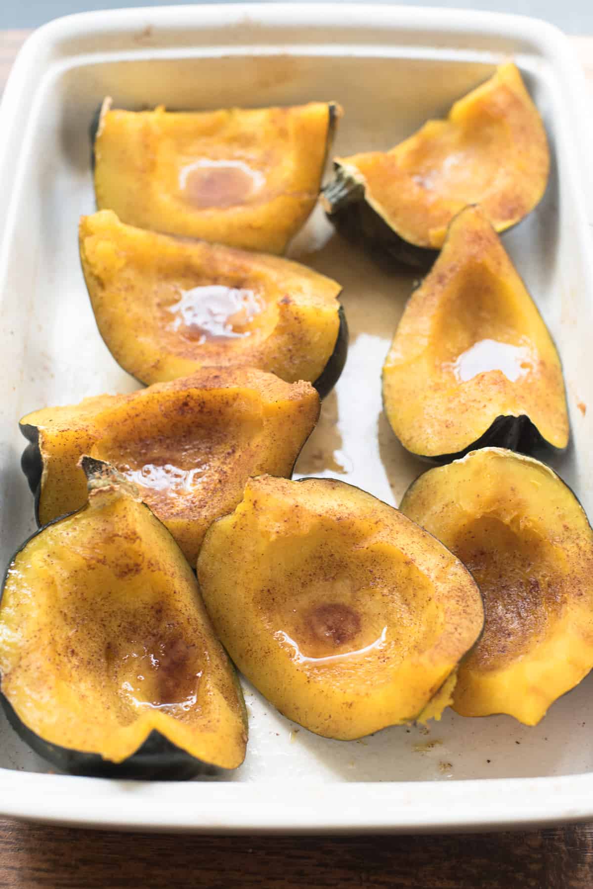 Baked acorn squash with brown sugar and butter in a white baking dish.