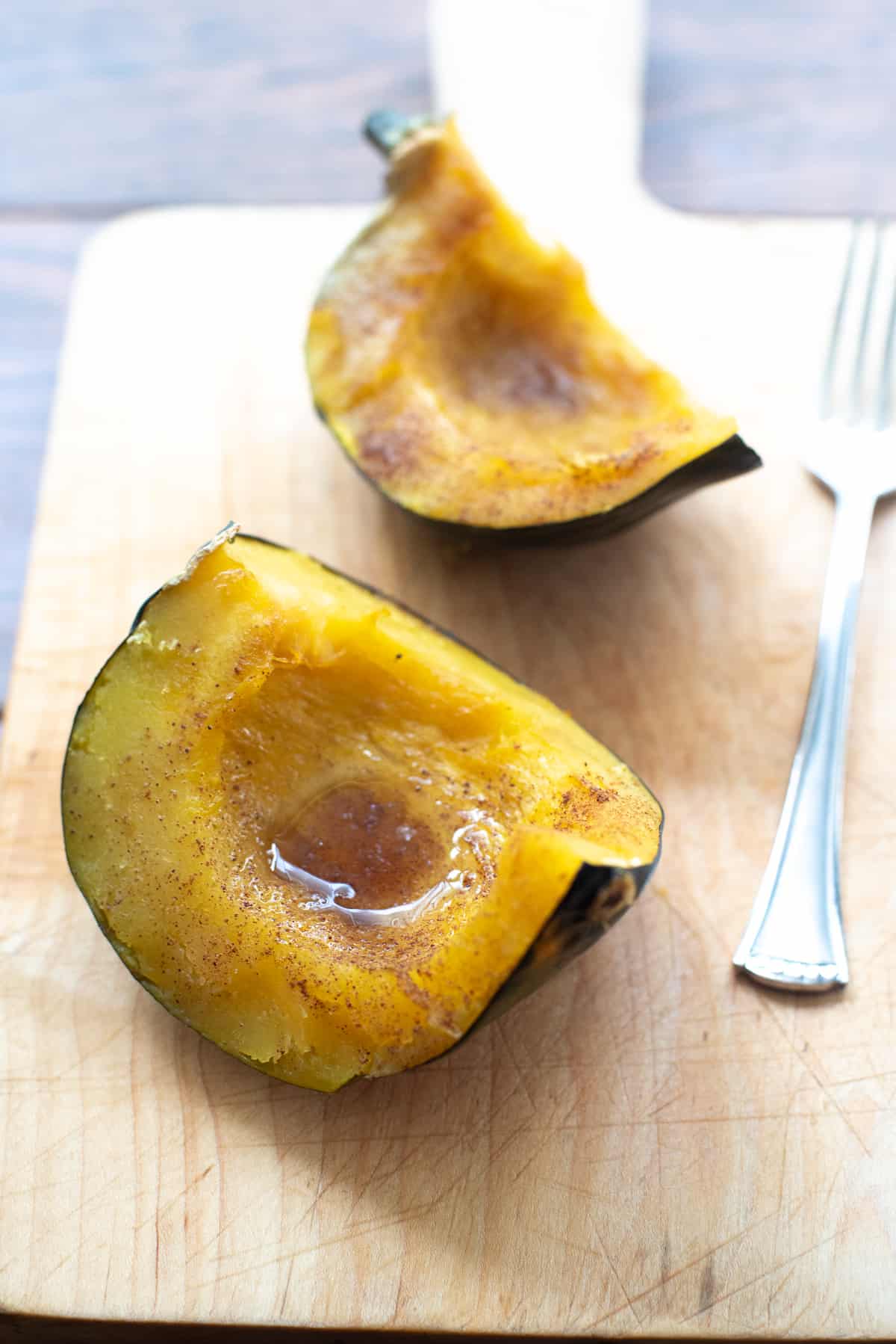 Two pieces of baked acorn squash on a cutting board with a fork.