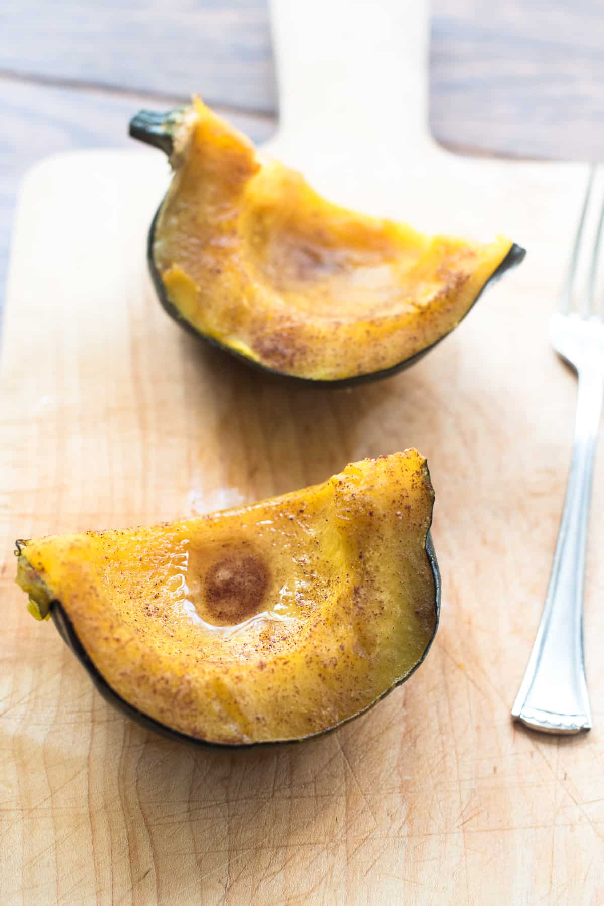 Two pieces of baked acorn squash placed skin side down on a cutting board with a fork.