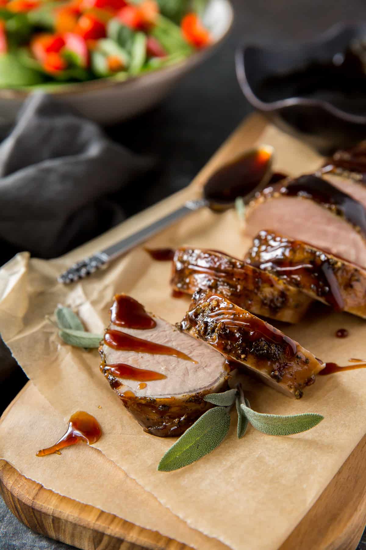 Sliced pork tenderloin on parchment paper next to a bowl of green salad.