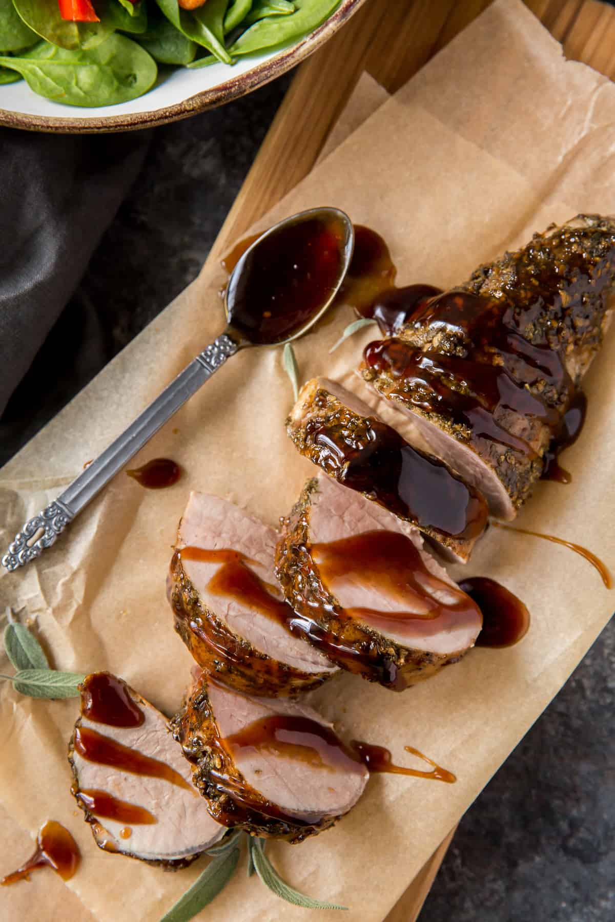 Sliced pork tenderloin on parchment paper next to a bowl of green salad.