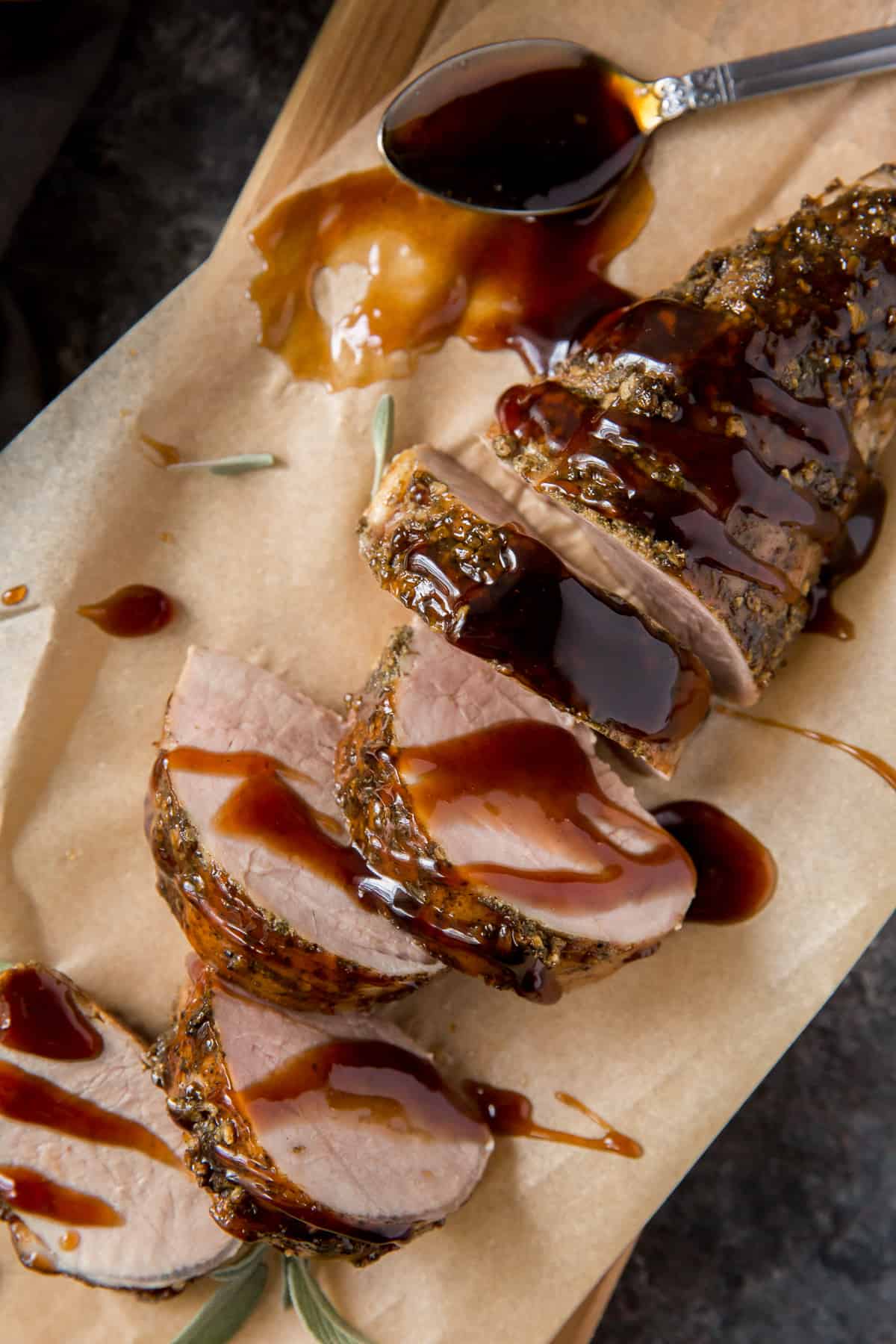 Sliced pork tenderloin drizzled with balsamic glaze on a parchment paper lined board.