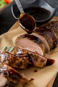 Balsamic glaze drizzling off a spoon on to sliced pork tenderloin.