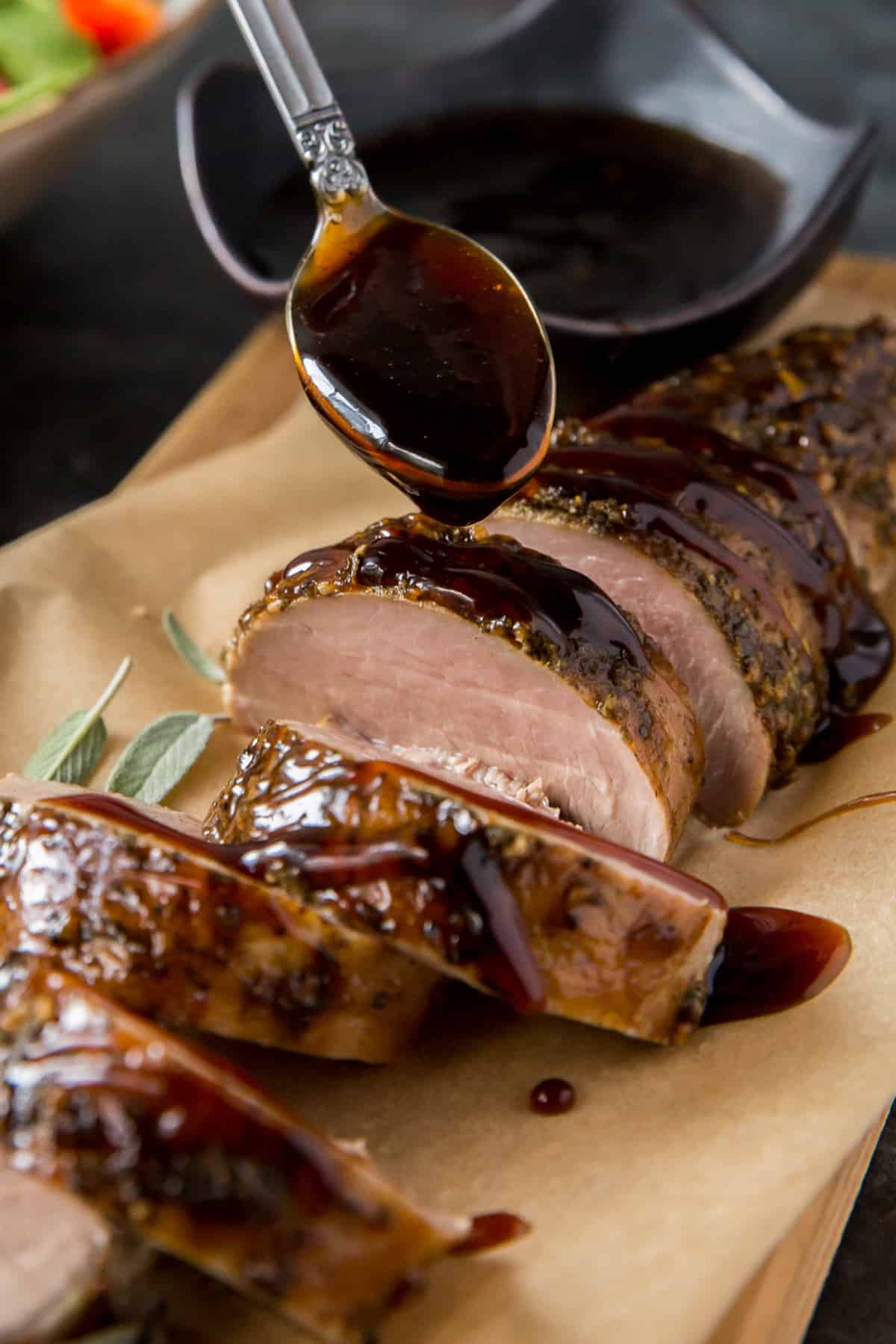 Balsamic glaze drizzling off a spoon on to sliced pork tenderloin.