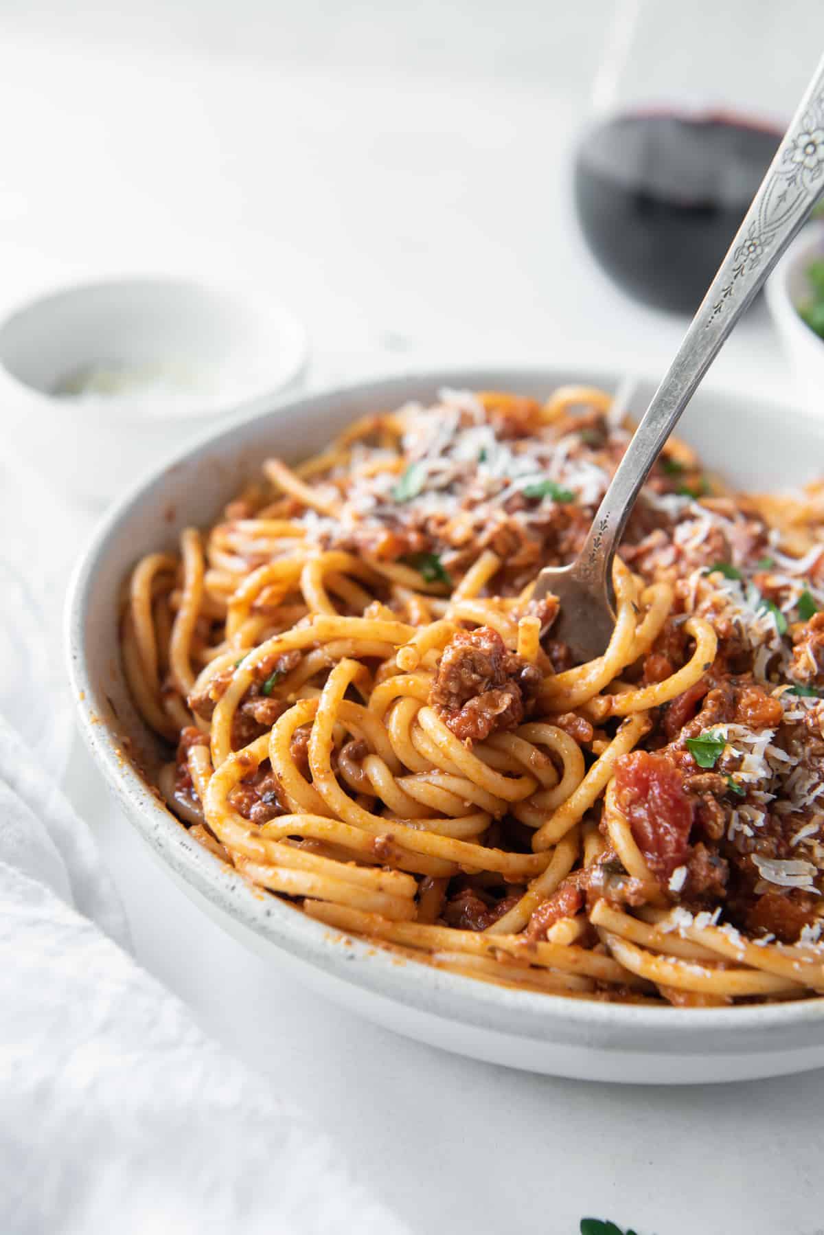 A fork twirling spaghetti with Bolognese sauce in a white bowl.
