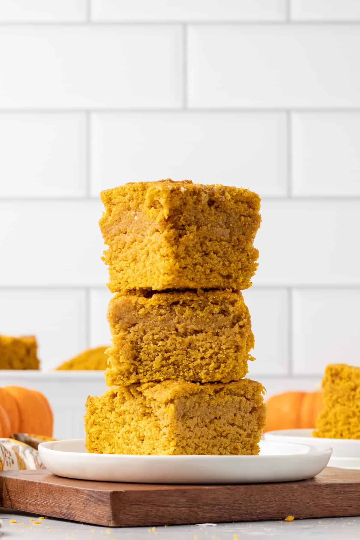 A stack of three slices of pumpkin cornbread on a white plate with a tile backsplash behind it.