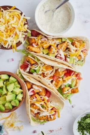 A top down shot of three chicken tacos with ranch taco sauce, avocado, cheese, and lettuce.