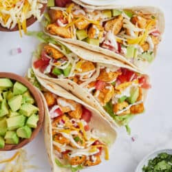 A top down shot of three chicken tacos with ranch taco sauce, avocado, cheese, and lettuce.