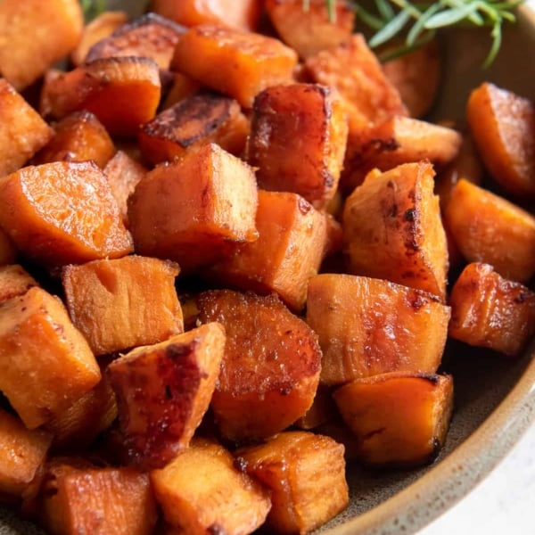 Chunks of roasted sweet potato in a serving bowl with a sprig of rosemary.