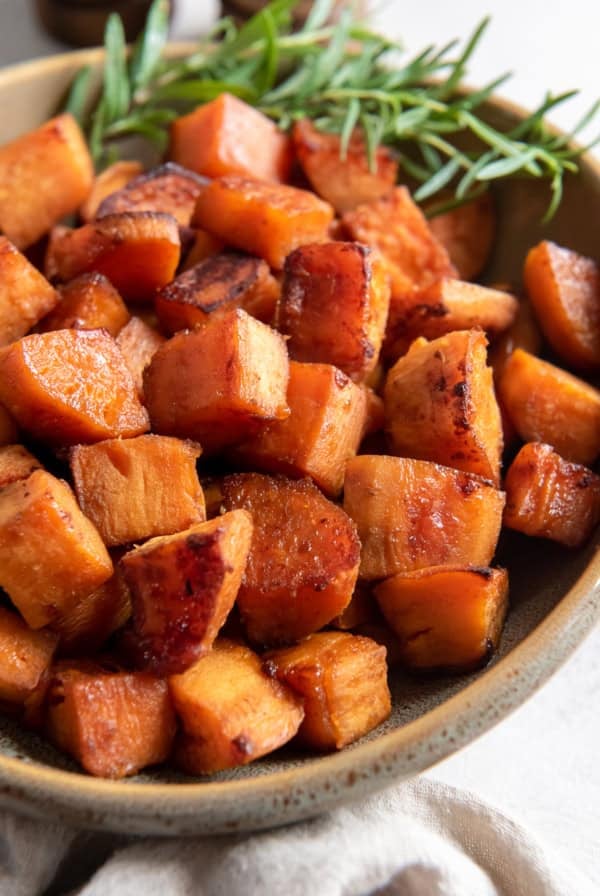 Chunks of roasted sweet potato in a serving bowl with a sprig of rosemary.