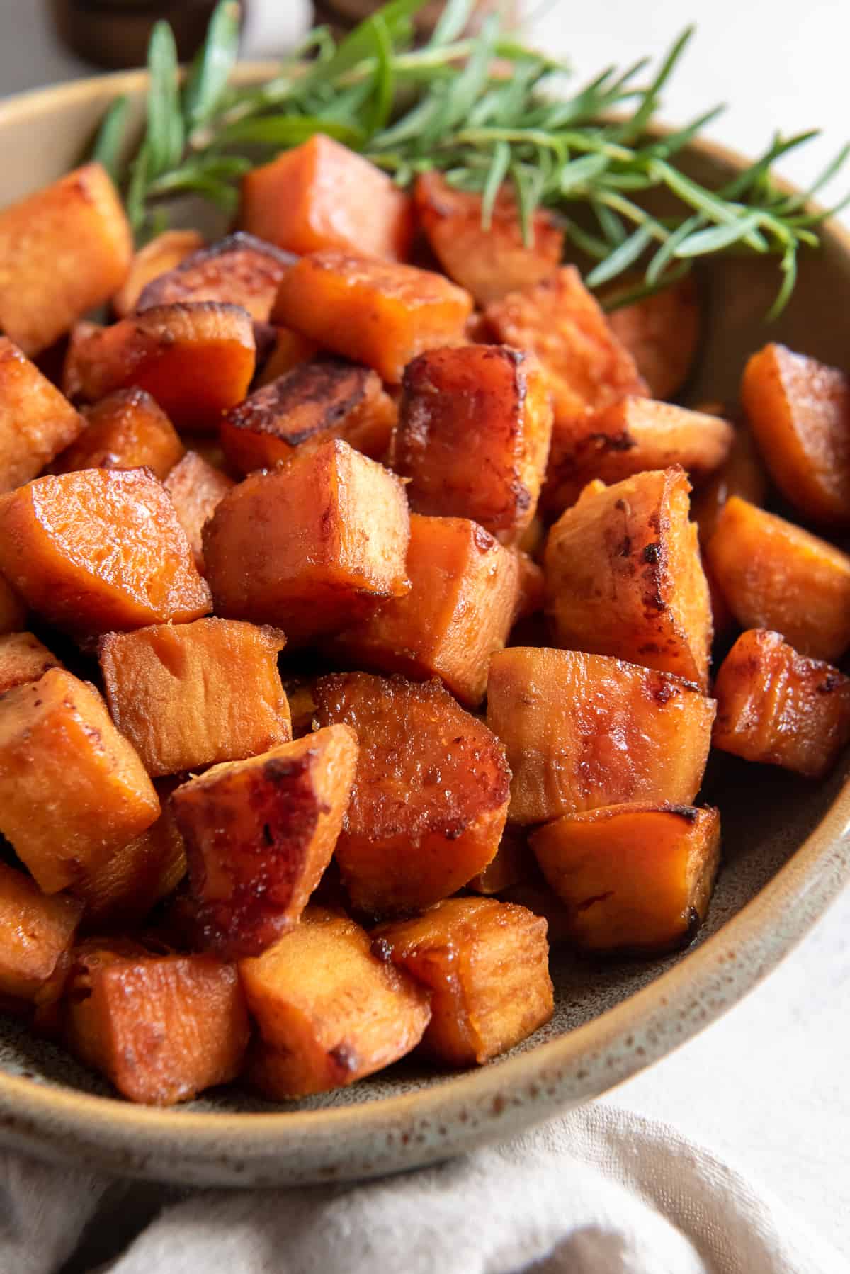 Chunks of roasted sweet potato in a serving bowl with a sprig of rosemary.