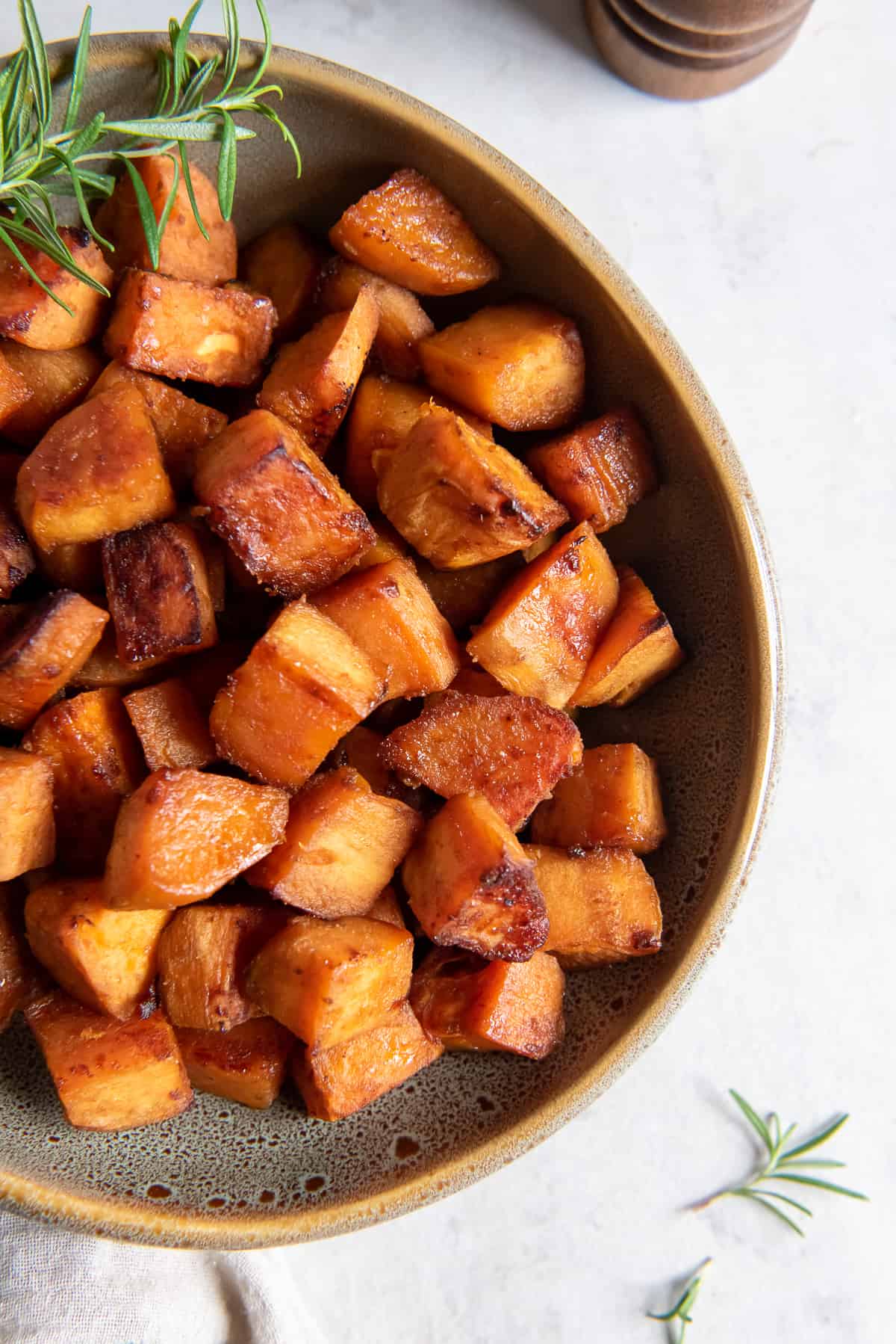 A top down shot of chunks of roasted sweet potato in a serving bowl with a sprig of rosemary.