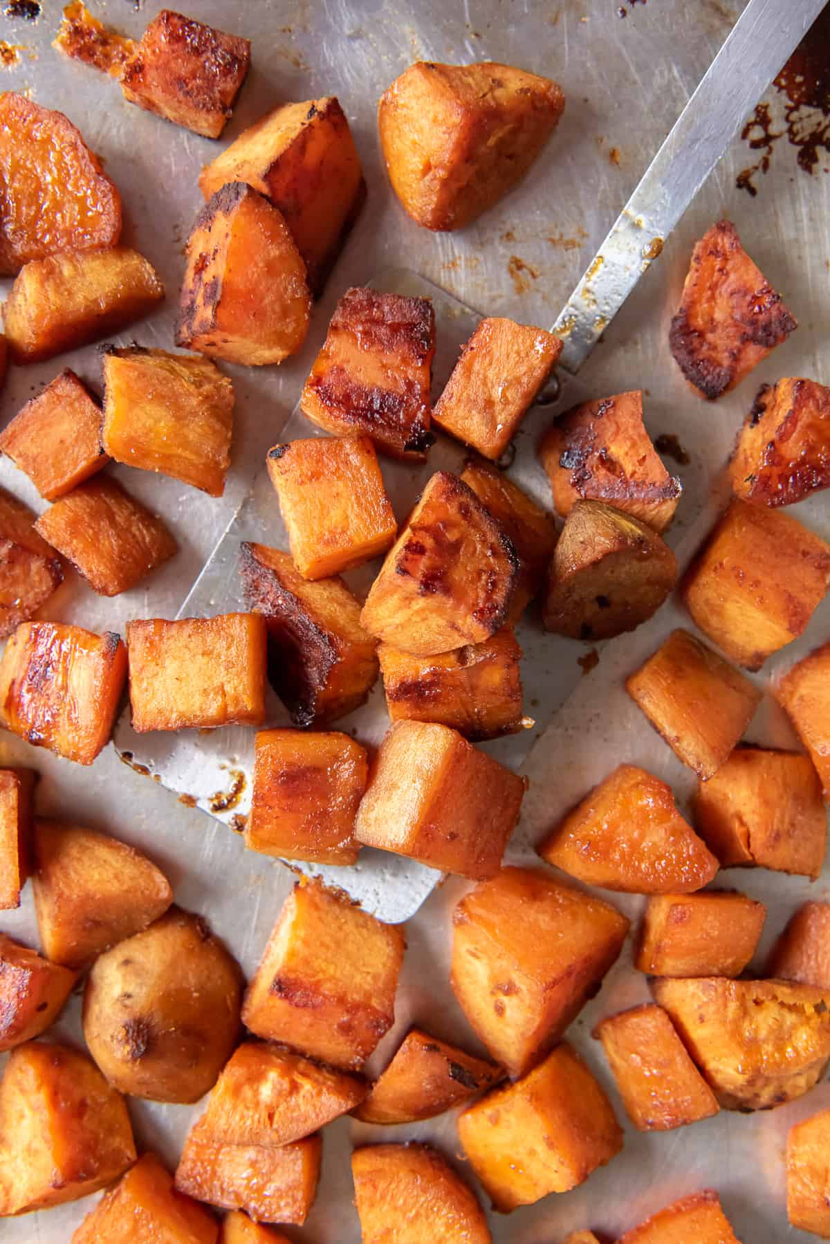 A close up top down shot of a spatula resting under roasted sweet potatoes on a baking sheet.