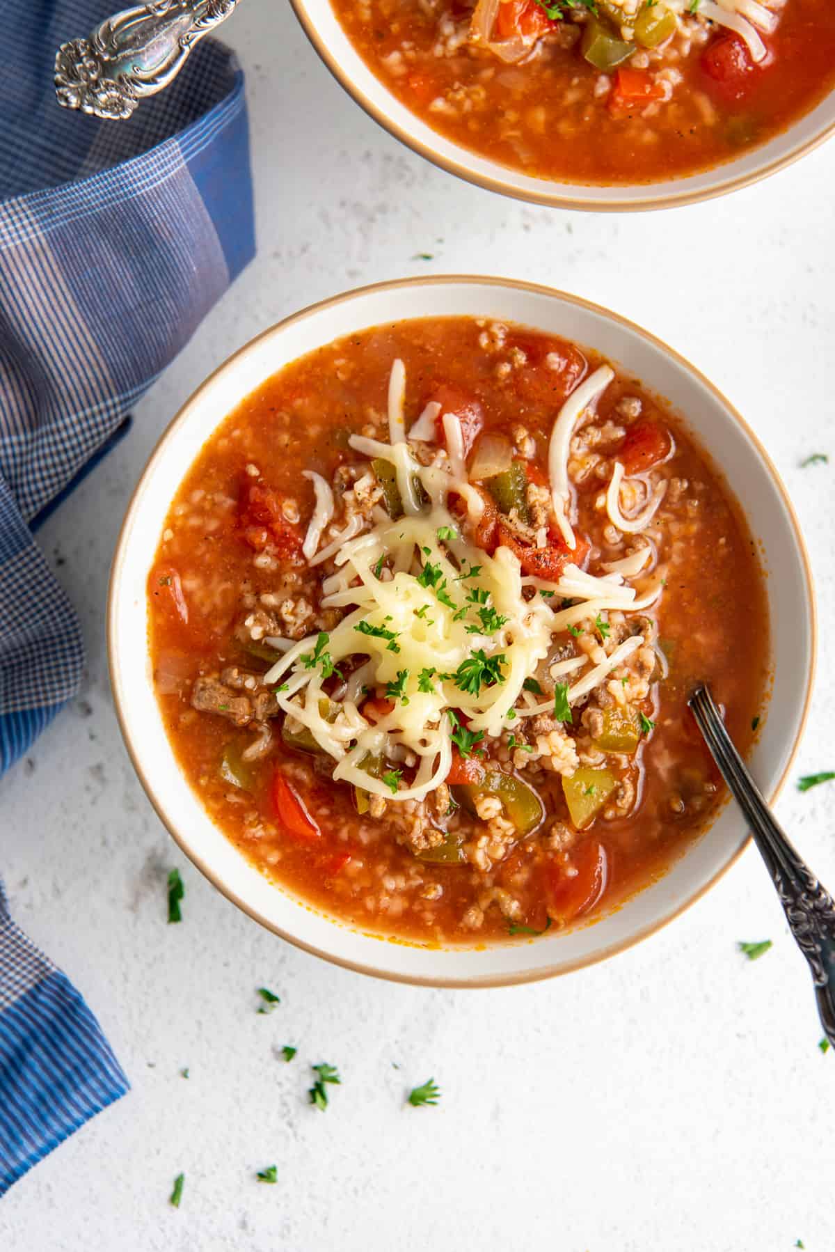 A top down shot of spoon resting in a bowl of soup with ground beef, rice, peppers, and topped with shredded cheese.