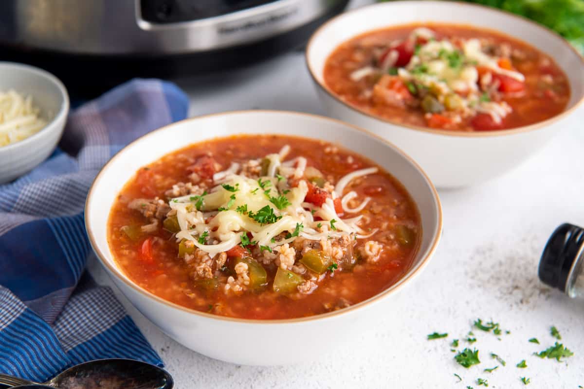 Two bowls of stuffed pepper soup topped with cheese next to a blue cloth.