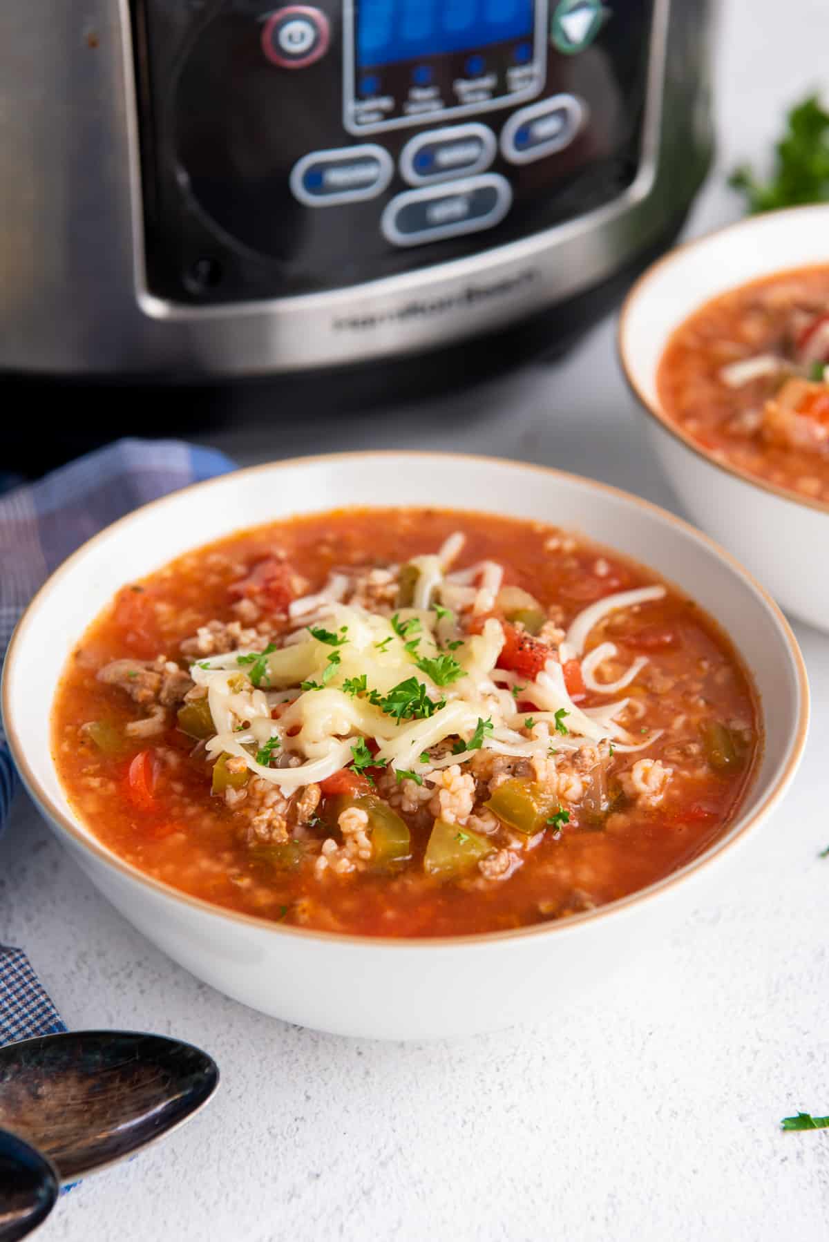 A bowl of stuffed pepper soup with a slow cooker in the background.