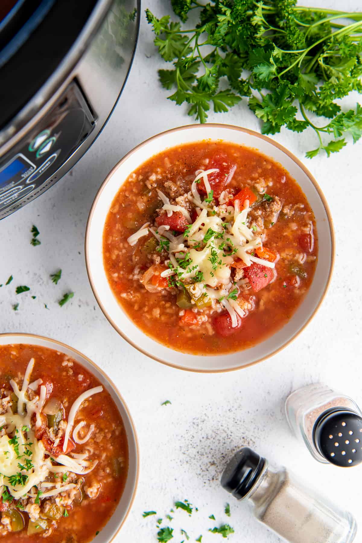 A top down shot of two bowls of stuffed pepper soup next to a crock pot and salt and pepper shakers.