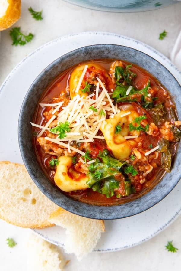 A top down shot of soup with tortellini and sausage in a bowl topped with Parmesan.