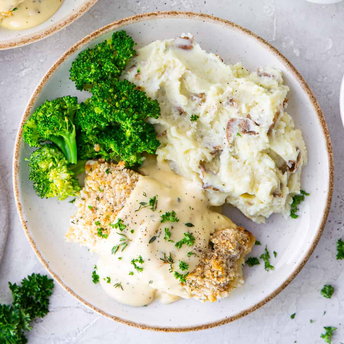 A top down close up shot of chicken with a creamy sauce on plates with mashed potatoes and broccoli.