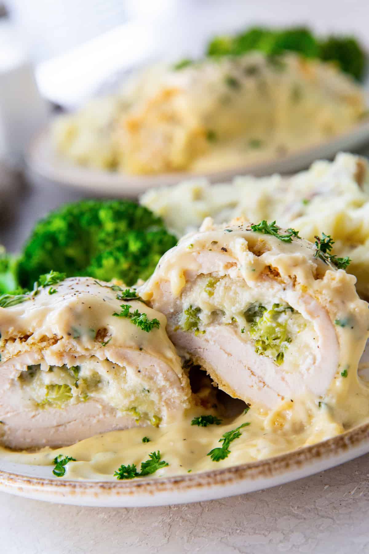 Breaded chicken breast with a broccoli cheese filling sliced in half and stacked on a white plate.