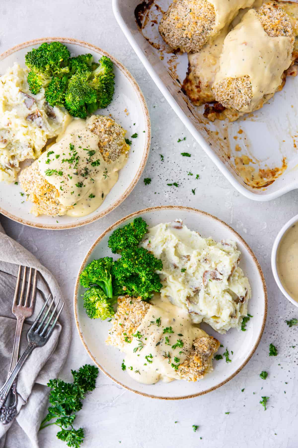 A top down shot of chicken with a creamy sauce on plates with mashed potatoes and broccoli.