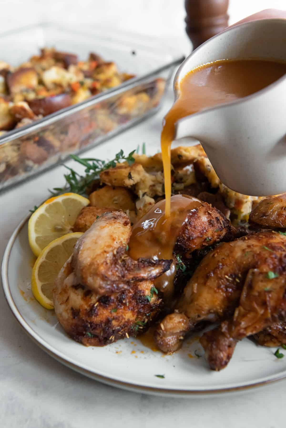 Gravy pouring from a gravy boat over cornish hens on a white plate.