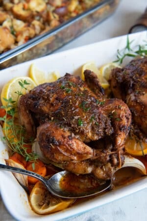 A roasted cornish hen in a baking dish with vegetables and lemon slices.