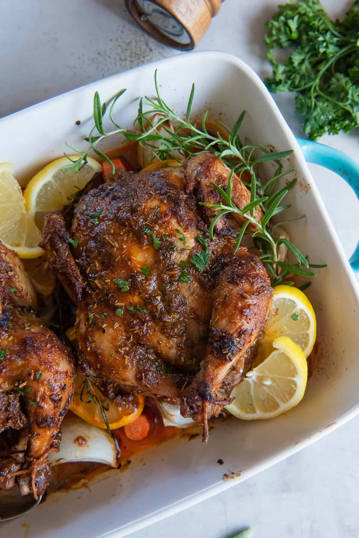 A close up of cornish games hens in a baking dish with vegetables, lemon, and sprigs of fresh rosemary.