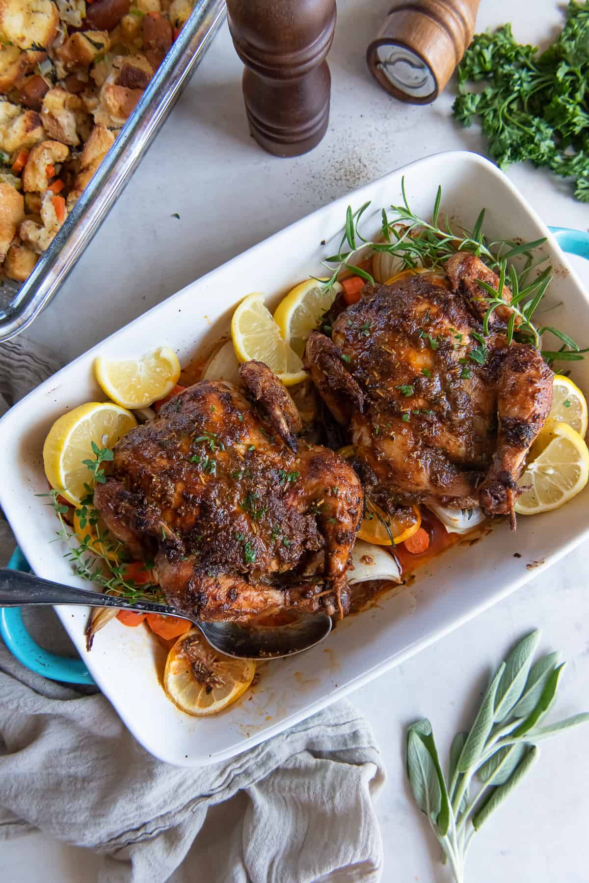 A top down shot of two roasted cornish game hens in a baking dish with a spoon.