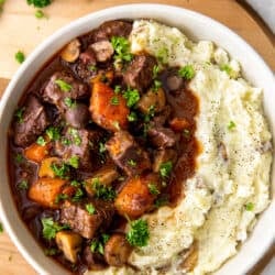 A top down view of a white bowl filled with beef burgundy and mashed potatoes.
