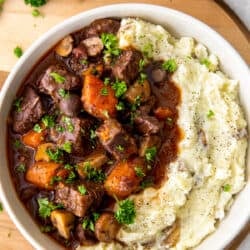 A top down view of a white bowl filled with beef burgundy and mashed potatoes.