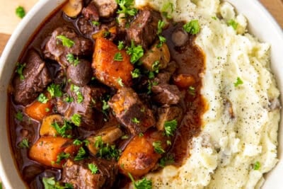 A top down view of a white bowl filled with beef burgundy and mashed potatoes.