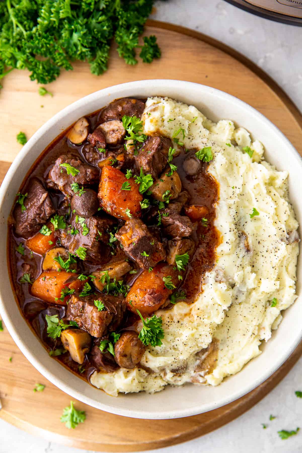 A top down view of a white bowl filled with beef burgundy and mashed potatoes.